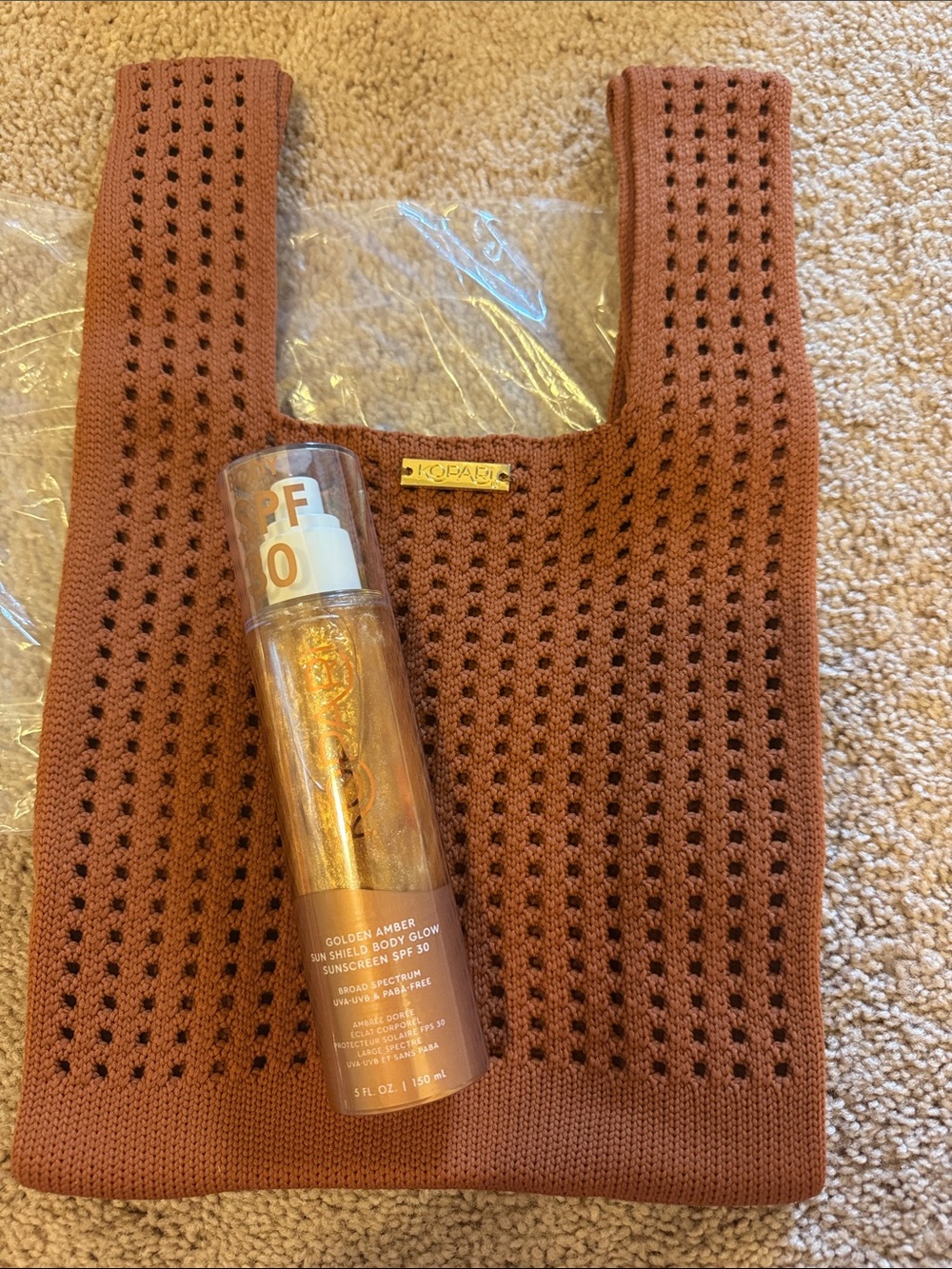 Kopari golden amber body glow sunscreen with rust knit tote